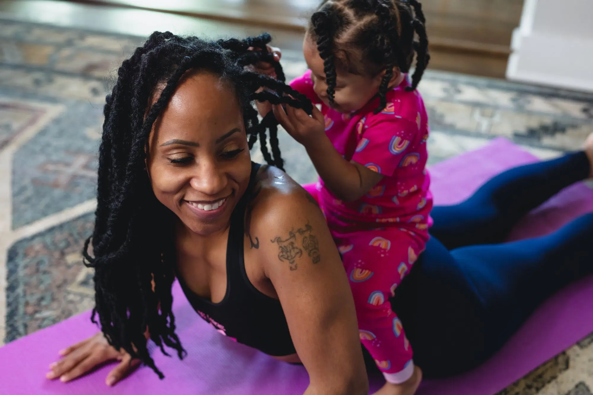 Woman doing yoga with a child sitting on her back playing with her hair. 