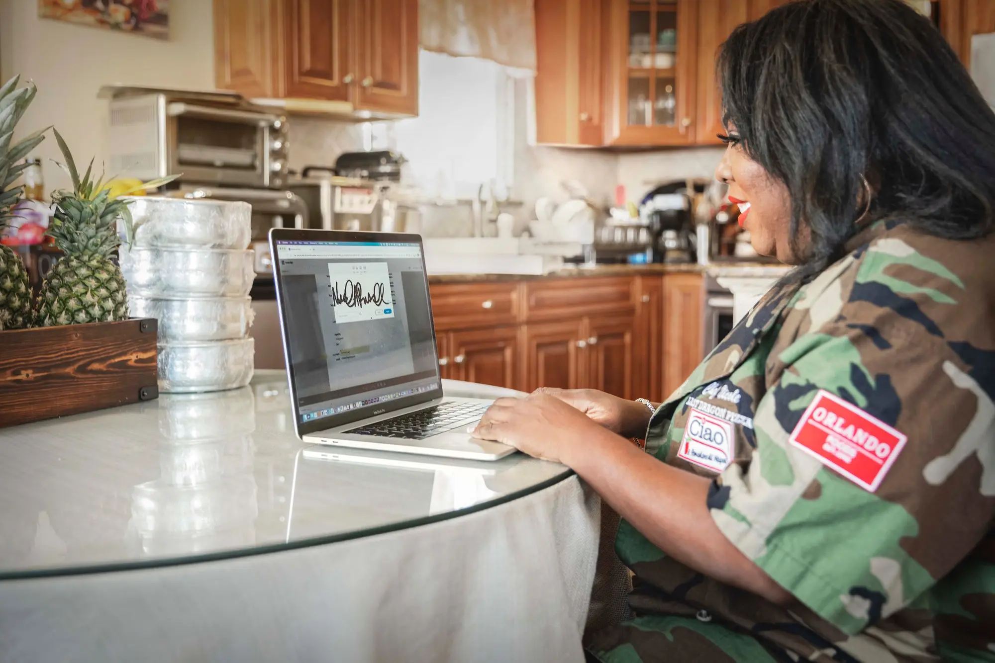 Woman sitting at a kitchen table with a laptop open to Adobe Acrobat. 
